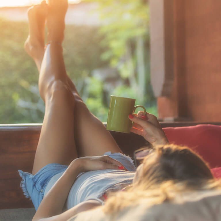Blasenentzündung durch Stress: Frau sitzt mit einer Tasse Tee am Fenster und sorgt für Entspannung.